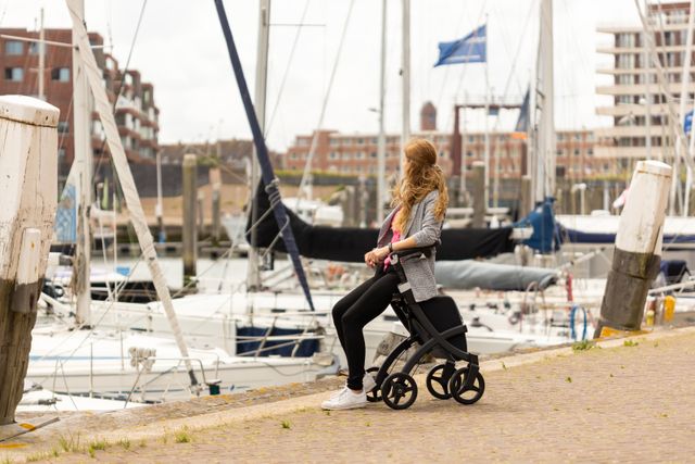 Jonge vrouw die aan een marina zit met een rollator. Stedelijke levensstijl scène.