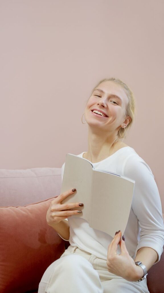 Vrolijke vrouw in het wit die op een pastelbank een boek vasthoudt en warmte en vreugde uitstraalt